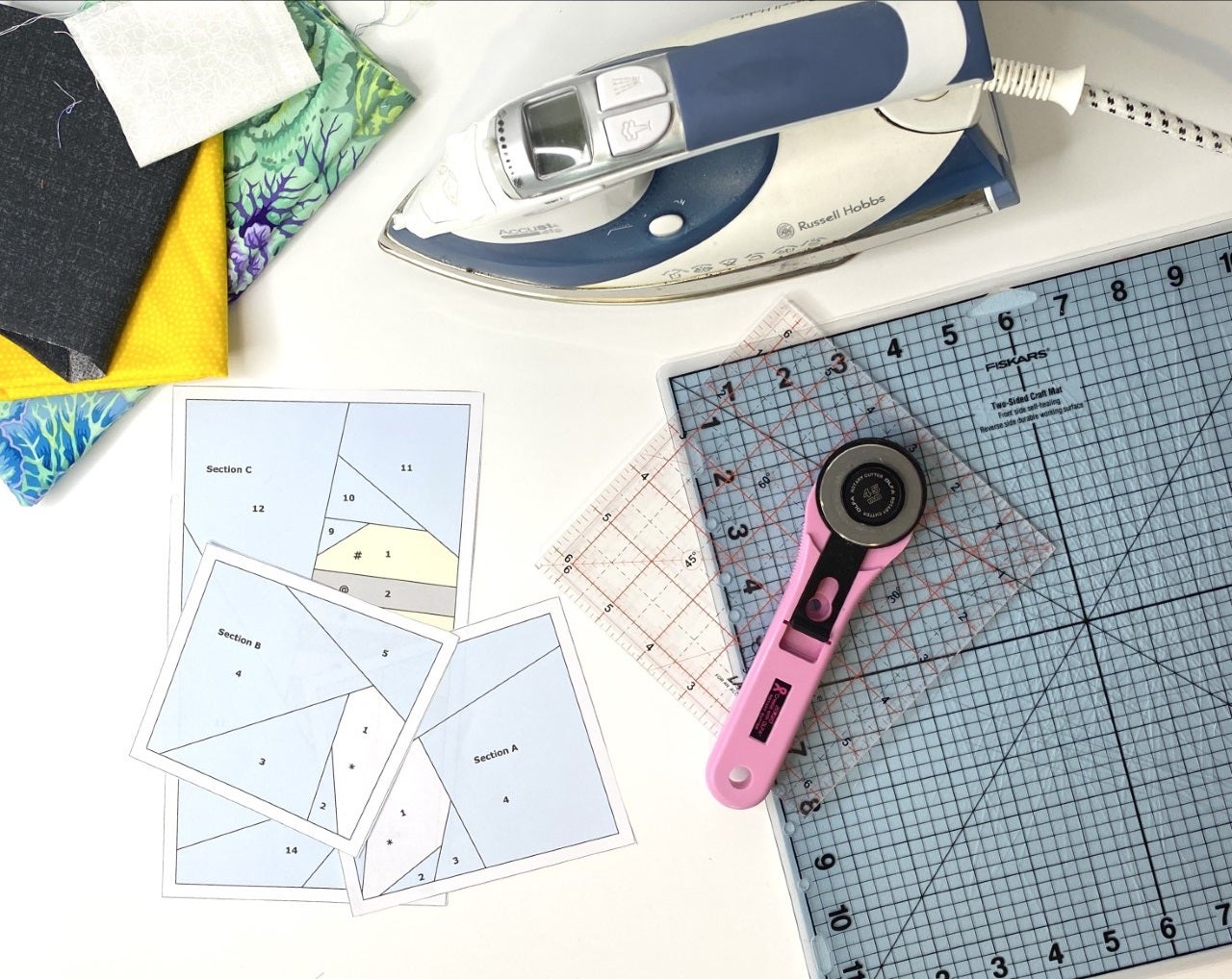 This quilt block is great when used to learn foundation paper piecing. This photo shows foundation paper piecing templates surrounded by quilting and sewing tools, such as fabric, cutting mat, ruler, and a rotary cutter.