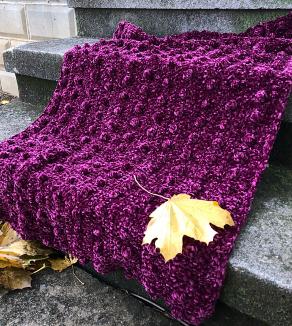 A purple blanket lies on stone steps. The rows of bobbles run horizontally as worked, but are shown vertically in the photo