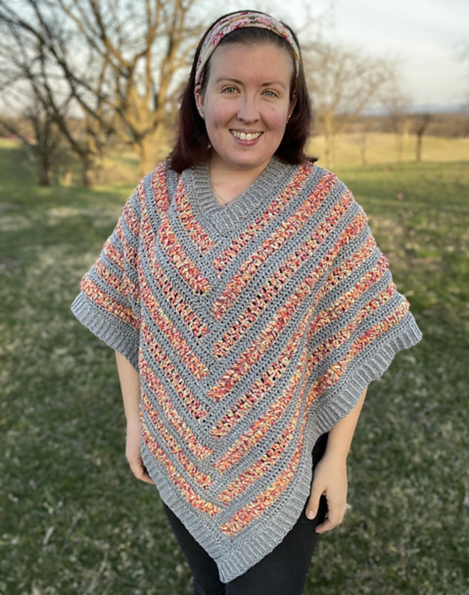 Ruth stands smiling with a light gray and pink/red striped poncho draped on her body.