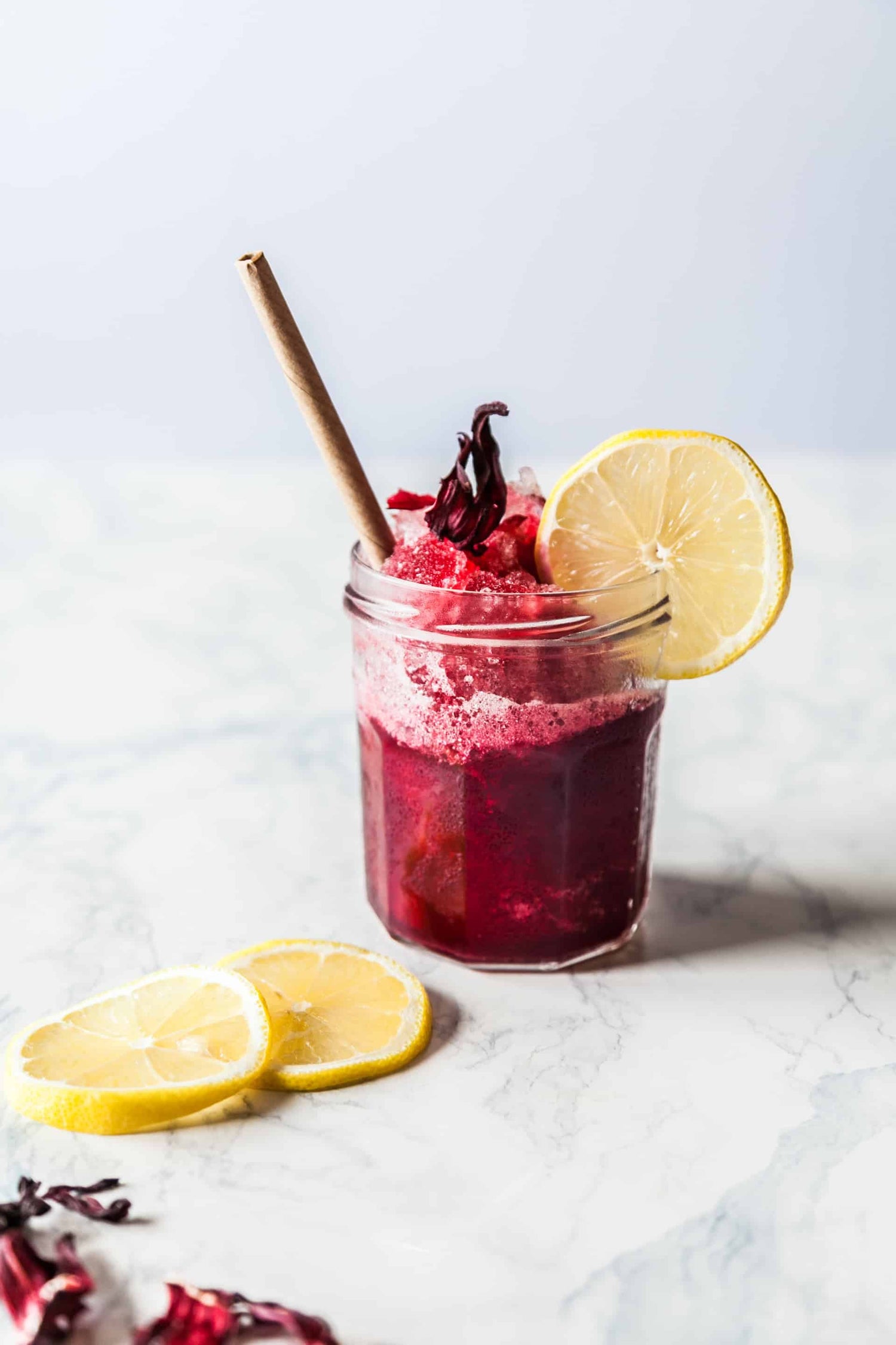 Beet smoothie in a glass jar atop a white marble counter, garnished with lemon.